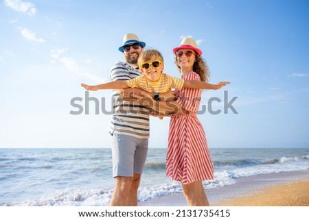 Happy family having fun on the beach. Mother and father holding son against blue sea and sky background. Summer vacation concept