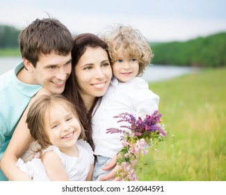 Happy Family Having Fun Outdoors In Spring Field Against Blurred Grass And Sky Background