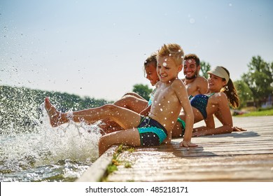 Happy Family Having Fun And Splashing Water With Their Feet On A Lake