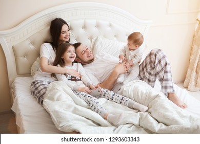  Happy Family Is Having Fun Together In Bedroom. Family Morning Concept.   Happy Parents With Two Kids Waking Up In Bed At Home. 