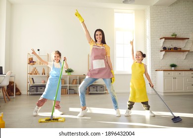 Happy Family Having Fun While Cleaning Their House. Cute Little Children Helping Mom Tidy Up Their Apartment. Smiling Young Mother And Daughters Dancing Together While Mopping The Floor At Home