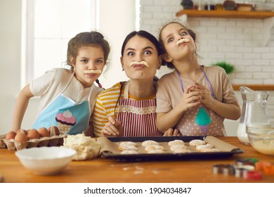 Happy Family Having Fun While Cooking. Little Kids And Young Mother Playing With Cookie Dough In The Kitchen. Portrait Of Cheerful Mom And Cute Children Making Funny Faces With Fake Pastry Mustaches