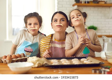 Happy family having fun while cooking. Children and mother baking cookies in the kitchen together. Cheerful young mom and little daughters playing with dough and making funny faces with fake mustaches