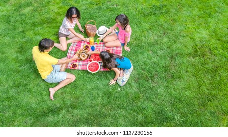 Happy Family Having Picnic In Park, Parents With Kids Sitting On Grass And Eating Healthy Meals Outdoors, Aerial View From Above