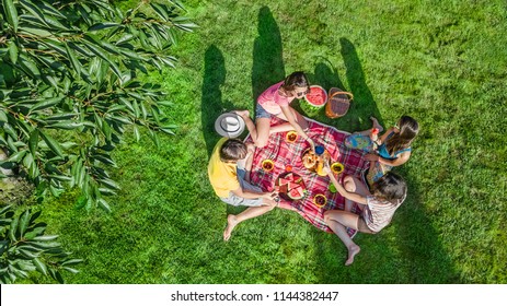 Happy Family Having Picnic In Park, Parents With Kids Sitting On Grass And Eating Healthy Meals Outdoors, Aerial View From Above