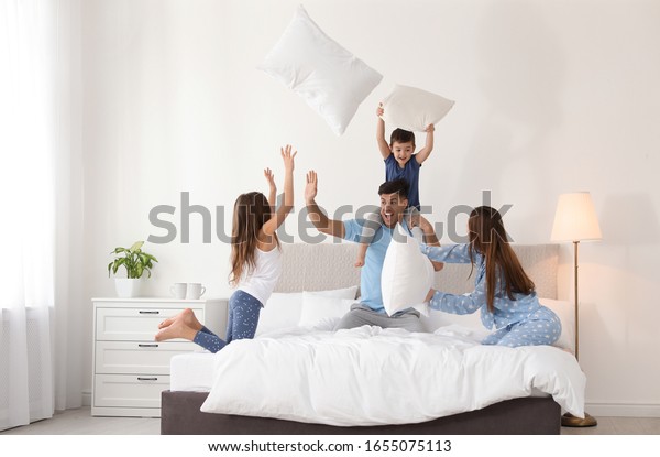 Happy family having\
pillow fight in bedroom