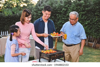 Happy Family Was Helping To Cook A BBQ In The Backyard. Family Enjoying A Barbecue Party Celebration In The Backyard Together