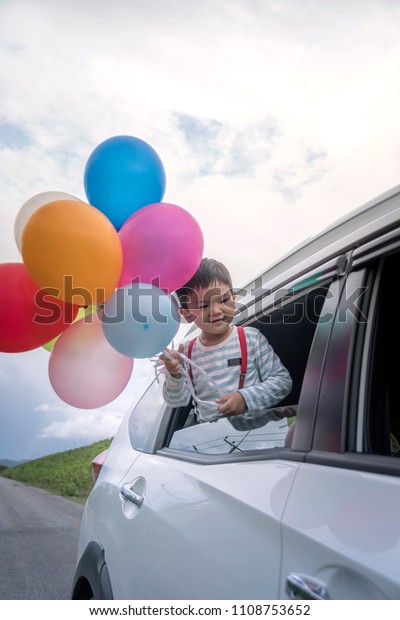 Happy family holding colorful balloons outdoor on\
the car having great holidays time on summer. Lifestyle, vacation,\
happiness, joy concept