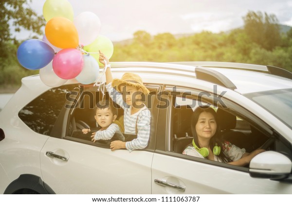 Happy family holding colorful balloons outdoor on\
the car having great holidays time on summer. Lifestyle, vacation,\
happiness, joy concept