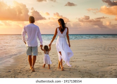 A Happy Family Holding Hands On Vacation Walks Down A Beach During Sunset Time