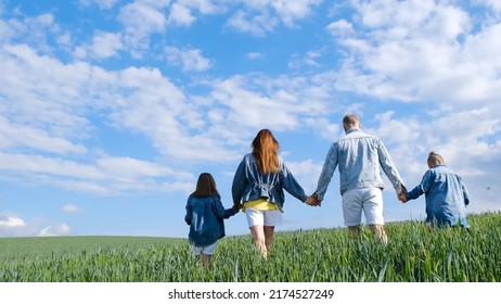 Happy Family Holding Hands Walking On A Green Field. Mom Dad And Daughter And Son Walk