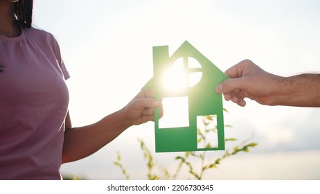 Happy Family Holding Paper House With Hands. House Happiness Concept. Big Family Dream Of Buying A House. Hands Holding Lifestyle A Paper House At Sunset Sun Glare. Mortgage Construction Concept