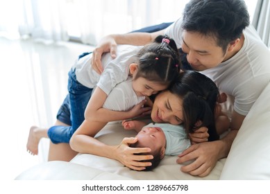 Happy Family At Home. Asian Father, Mother And Sister On Sofa Are Smiling, Laughing And Playing With Newborn Baby, New Member Of Their Family. They Spent A Great Time Together. Happy Family Concept.