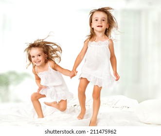 Happy Family At Home. Kids Twin Sisters Jumping On The Bed, Playing And Laughing