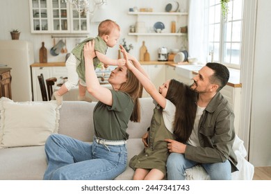 Happy family at home. Mother father two children daughters relaxing on sofa indoor. Mom dad parents baby girls kids relax playing having fun together. Family smiling laughing enjoying tender moment - Powered by Shutterstock