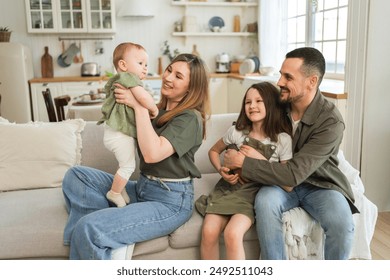 Happy family at home. Mother father two children daughters relaxing on sofa indoor. Mom dad parents baby girls kids relax playing having fun together. Family smiling laughing enjoying tender moment - Powered by Shutterstock