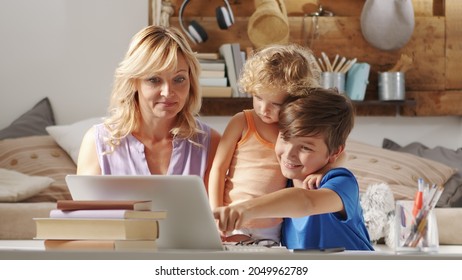 Happy Family At Home, Mother With Son And Daughter Have Fun Using Computer, Parent With Children Browsing Internet On Laptop, Child Student Shows Something Pointing At The Monitor