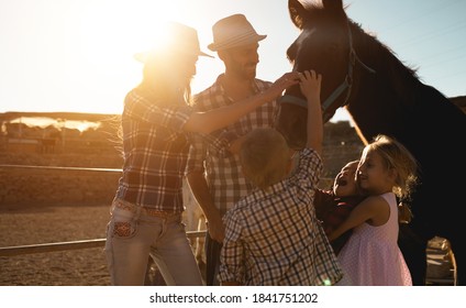 Happy family with horse having fun at farm ranch - Parentc and children cuddling animal pet at sunset outdoor - Love and youth concept - Soft focus on father face - Powered by Shutterstock