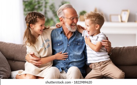 Happy family joyful little children hugging   grandfather   and laughs while sitting together on sofa  on grandparents day