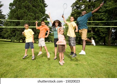 A happy family jump at the same time together, with rackets in air. - horizontally framed