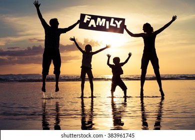 Happy family jumping on the beach at the sunset time. Parents hold in the hands  inscription "Family". Concept of happy family.