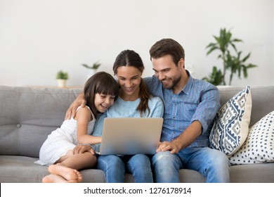 Happy Family With Kid Girl Having Fun Using Laptop Together Sitting On Sofa, Parents And Child Daughter Laughing Relaxing At Home With Computer Watching Funny Internet Video, Making Online Call