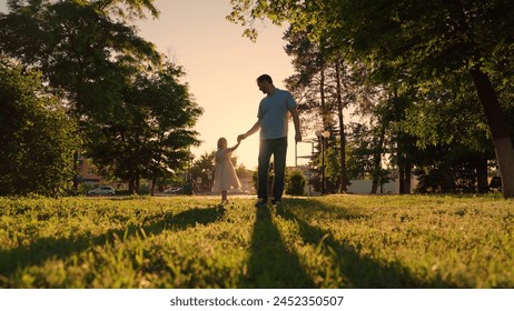 Happy family, kid, go towards sun, holding hands in city park at sunset. Childhood future, family game. Family, dad little daughter play together, child holding father hand. Parents, kid sun nature - Powered by Shutterstock