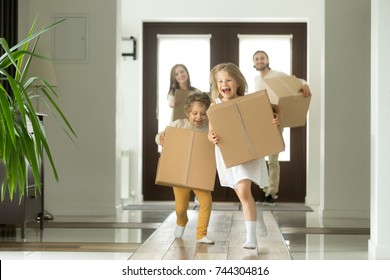 Happy Family With Kids Bought New Home, Excited Children Funny Girl And Boy Holding Boxes Running Into Big Modern House, Helping Parents With Belongings, Moving Day Concept, Mortgage And Relocation 