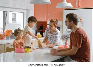 Happy Family With Kids Cooking On Modern Kitchen. Children Cutting Fruit Salad, Preparing Food With Mother And Father. Healthy Eating At Home. Communication And Support Daughter, Son