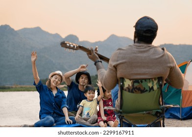 happy family with kids enjoy singing songs playing music outdoor camping area with the mountain and river beauty in nature, diverse friends travelers spend time together during holiday vacation trip - Powered by Shutterstock