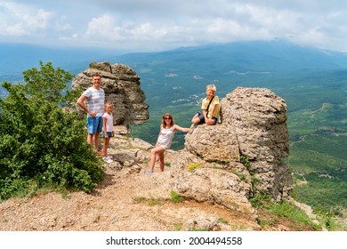 Happy Family With Kids In Green Meadow Looking At Camera. Concept Of Family Travel In Mountains. Father, Mother, Daughter And Son Have Fun In Nature