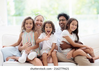 Happy family with kids at home. Parents and children sitting on white couch in sunny living room. Mother, father, son and daughter play and laugh. Young beautiful interracial couple in new house. - Shutterstock ID 2162779621