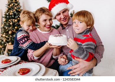 Happy Family With Kids Sitting At Christmas Table Holding Eating Cake Celebrating New Year