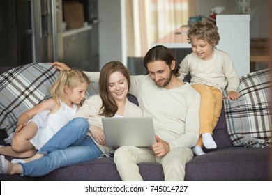 Happy Family With Kids Using Laptop Sitting On Sofa At Home, Smiling Parents And Son Daughter Relaxing On Couch Holding Computer, Man Woman With Children Shopping Together Online In Cozy Living Room