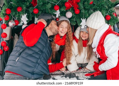 Happy Family Kissing Kids On Christmas Family Party, Sisters Are Laughing. Family Have Fun In Car Trunk Among Red Holiday Decoration,