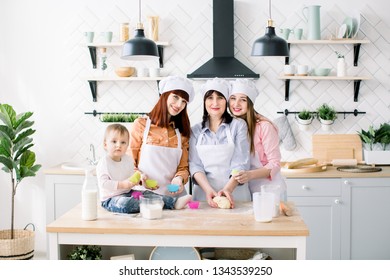 Happy Family In The Kitchen. Young Woman And Her Sister, Middle Aged Woman And Little Cute Daughter Cooking Cupcakes For Mothers Day, Casual Lifestyle Photo Series In Real Life Interior