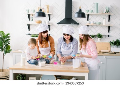 Happy Family In The Kitchen. Young Woman And Her Sister, Middle Aged Woman And Little Cute Daughter Cooking Cupcakes For Mothers Day, Casual Lifestyle Photo Series In Real Life Interior