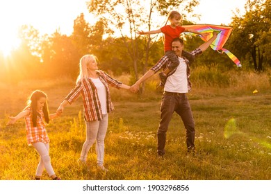 Happy Family With A Kite Playing At Sunset In The Field