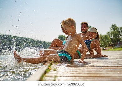 Happy family at a lake having fun and splashing water in summer - Shutterstock ID 563093056