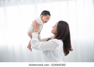 Happy Family. Laughing Mother Lifting Her Adorable Newborn Baby Son In Air, Copy Space. Asian Mother Lifting And Playing With Newborn Baby, Health Care Family Love Together. Asian Girl Lifestyle.