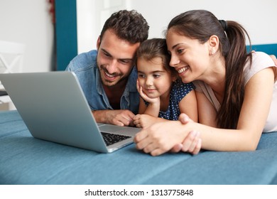 Happy family lies on bed and watching something on laptop. - Powered by Shutterstock