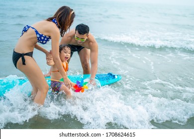 Happy family lifestyle concept.Young mother with kids surfing position and splashing with fun in breaking waves.Summer travel, water sport outdoor activities,swimming lessons on tropical beach holiday