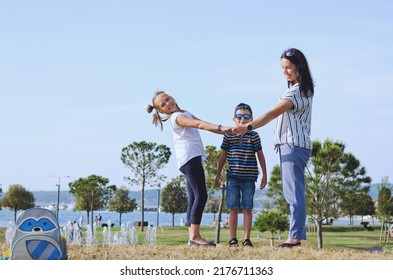 Happy Family Lifestyle And Holiday Concept. Mother, Little Boy, Girl Sitting, Walking In Old City, Street. Laughing On A Summer Sunny Day. Having Fun