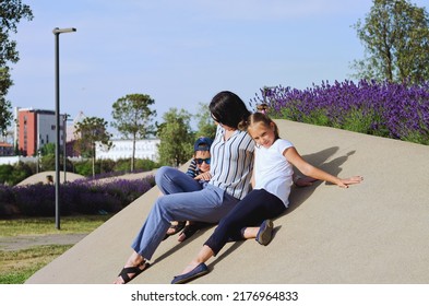 Happy Family Lifestyle And Holiday Concept. Mother, Little Boy, Girl Sitting, Walking In Old City, Street. Laughing On A Summer Sunny Day. Having Fun