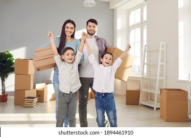 Happy Family With Little Children Celebrating Moving Into New Home. Portrait Of Smiling Young Couple With Excited Kids Standing In Room With Packed Boxes. Buying House, Real Estate, Mortgage Concept