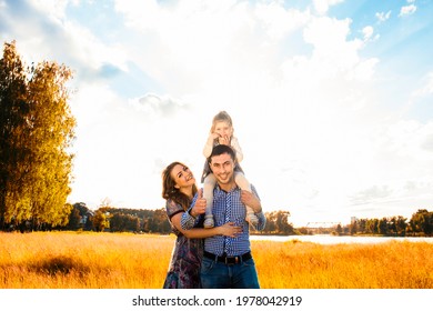 Happy Family With A Little Daughter In A Field In Nature, Looking Ahead, In The Rays Of The Sunset.