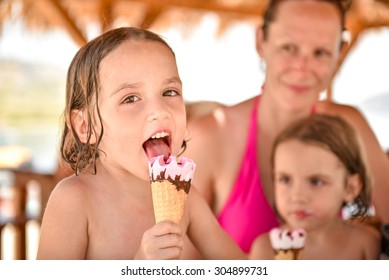 Happy family with little girl smiling and eating ice cream and mother and sister in the background. They are laughing, eating ice cream in beach hut after swimming in tropical sea. Vacation, lifestyle - Powered by Shutterstock