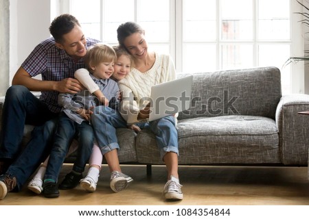 Happy family with little kids enjoying using application on laptop together, smiling parents spending time with children son and daughter having fun watching video or doing internet shopping at home