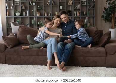 Happy family with little kids sit on sofa using digital tablet, buying on e-commerce retail web services, choose goods toys via website online shop. Modern tech usage, generation, leisure fun concept - Powered by Shutterstock