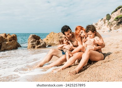 Happy family with little kids sitting on sandy seashore against waving sea and rocky formations enjoying a sunny day - Powered by Shutterstock